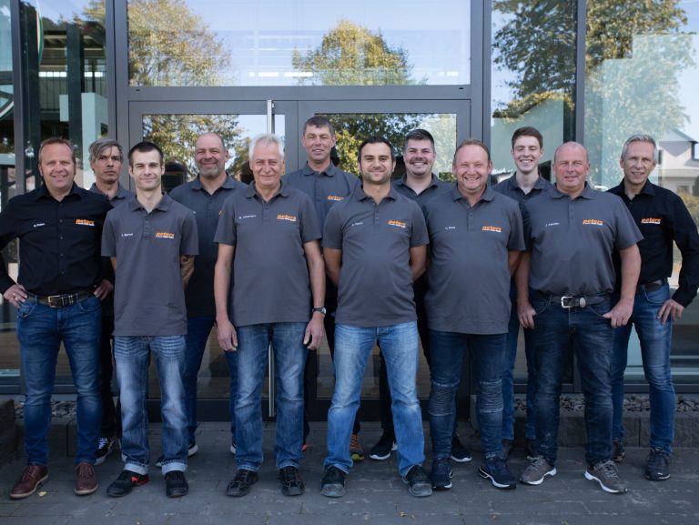 Bildrechte: Anton Peters GmbH & Co. KG Gruppfoto von zehn Mitarbeitern der Firma Peters in grauen T-Shirts mit dem Firmenlogo, die lächeln und vor einer Glasfassade stehen.